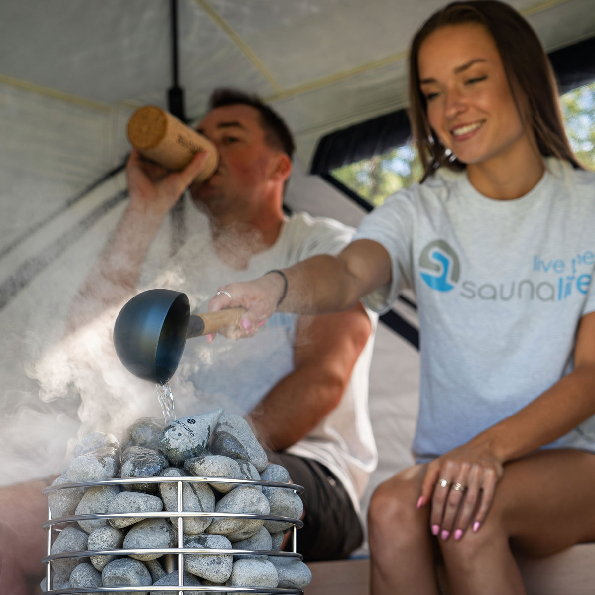 Two bathers inside a SaunaTrekker tent pouring water on the Titan SL1 gas heater
