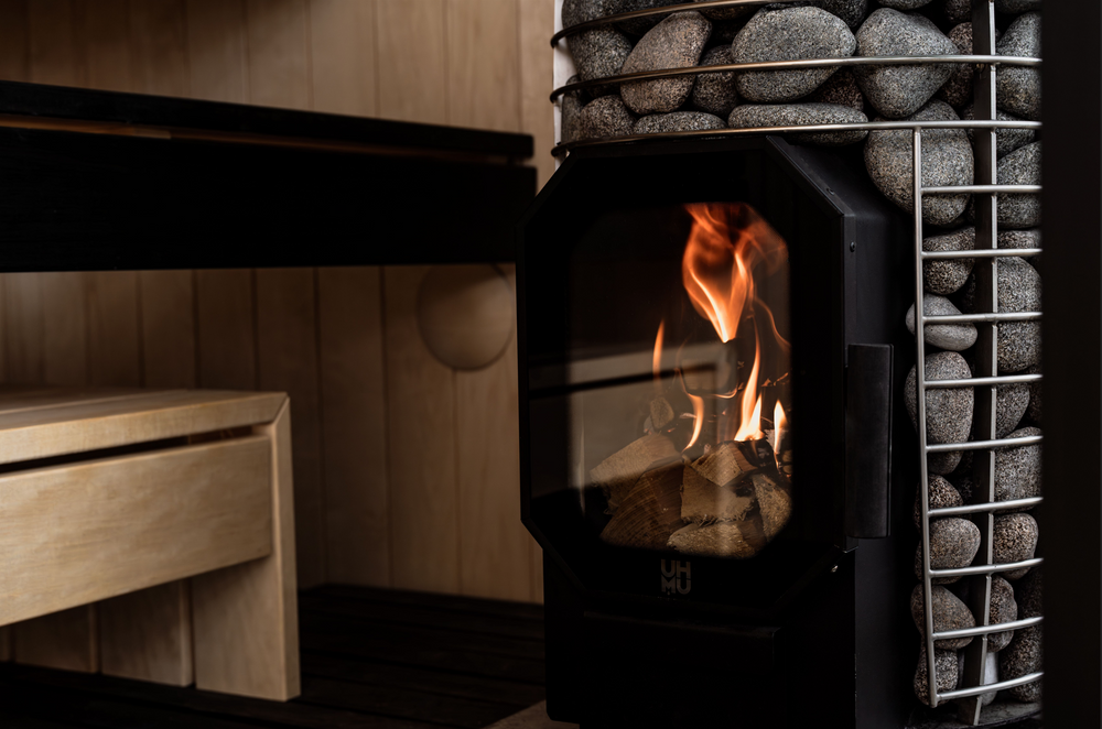 Wood-burning sauna stove alight beside a stone-filled heater guard
