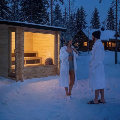 Canadian Timber Avalon sauna lit from within on a winter night with two people in robes standing in the snow