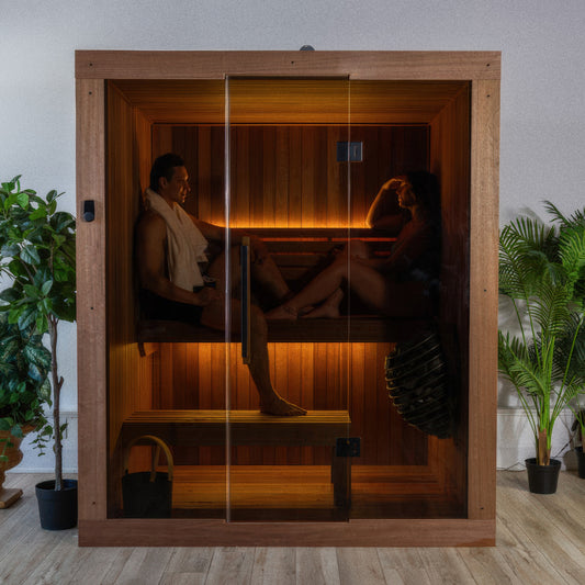 Canadian Timber Element Loft Indoor Sauna — two people on the upper bench behind the full glass front, set up in a living room